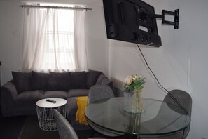 A living room with a sofa, a glass table, a remote control, a flower vase, and a mounted TV. - Modern 2Bed Apartment Sleeps 6 (Ilkeston)