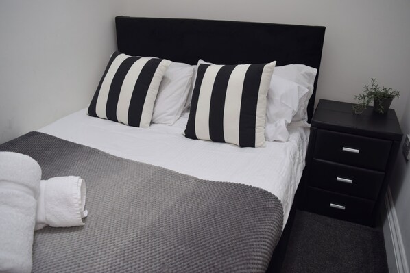 Una cama bien hecha con almohadas a rayas, una manta gris y una toalla blanca.