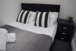 Ein ordentlich bezogenes Bett mit gestreifter Bettwäsche, einer grauen Decke und einem weißen Handtuch.