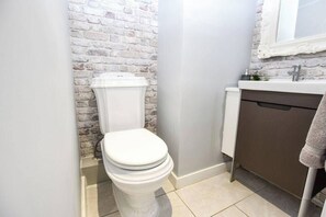 Une salle de bain avec des toilettes blanches, un lavabo avec un miroir et un sol carrelé.