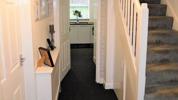 A hallway with a staircase, a door leading to a room with a window, and a small table with a vase. - Spacious 4-Bedroom Family Home Sleeps 8 (Bordon)