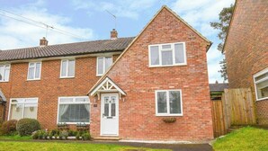 A two-story brick house with a white door, a small front garden, and a visible number '19' on the door. - Spacious 4-Bedroom Family Home Sleeps 8 (Bordon)