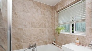 A bathroom with a bathtub, a sink, a window with blinds, and a potted plant. - Spacious 4-Bedroom Family Home Sleeps 8 (Bordon)