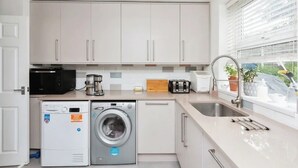 A modern kitchen with white cabinets, a washing machine, a microwave, a toaster, and a sink. - Spacious 4-Bedroom Family Home Sleeps 8 (Bordon)