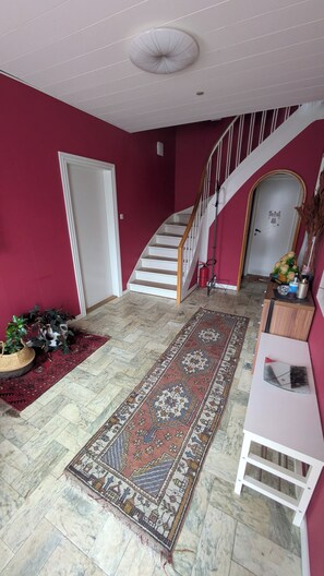 Eine Treppe führt zu einer Empore mit einer roten Wand, einem gemusterten Teppich und einem weißen Konsolentisch.