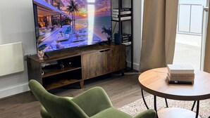 A modern living room with a flat-screen TV, a green armchair, a small round table, and a bookshelf. - Central 1-Bed Apt, Sleeps 2 w/ Underground Parking (Birmingham)