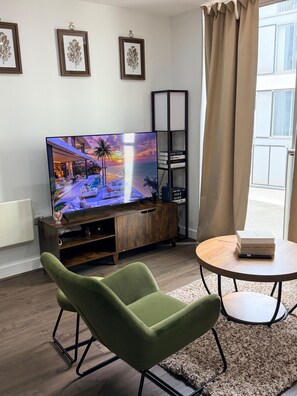 A modern living room with a flat-screen TV, a green armchair, a small round table, and a bookshelf. - Central 1-Bed Apt, Sleeps 2 w/ Underground Parking (Birmingham)