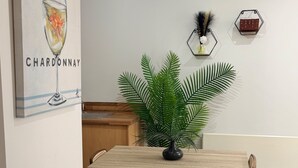 A dining area with a wooden table, two wicker chairs, a potted plant, a ceiling light, and hexagonal wall decorations. - Central 1-Bed Apt, Sleeps 2 w/ Underground Parking (Birmingham)
