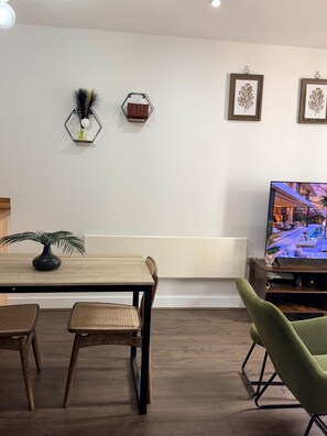 Un salon moderne comprenant une table à manger, des chaises, un téléviseur et des œuvres d’art décoratives au mur.