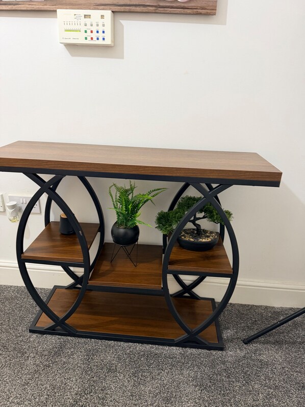 Ein hölzerner Konsolentisch mit schwarzen Metallbeinen und Regalen, stehend auf einem Teppichboden.
