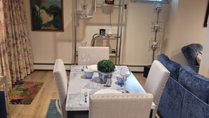 Un coin repas avec une table dressée pour quatre personnes, un canapé bleu, un tableau et une fenêtre avec des stores.
