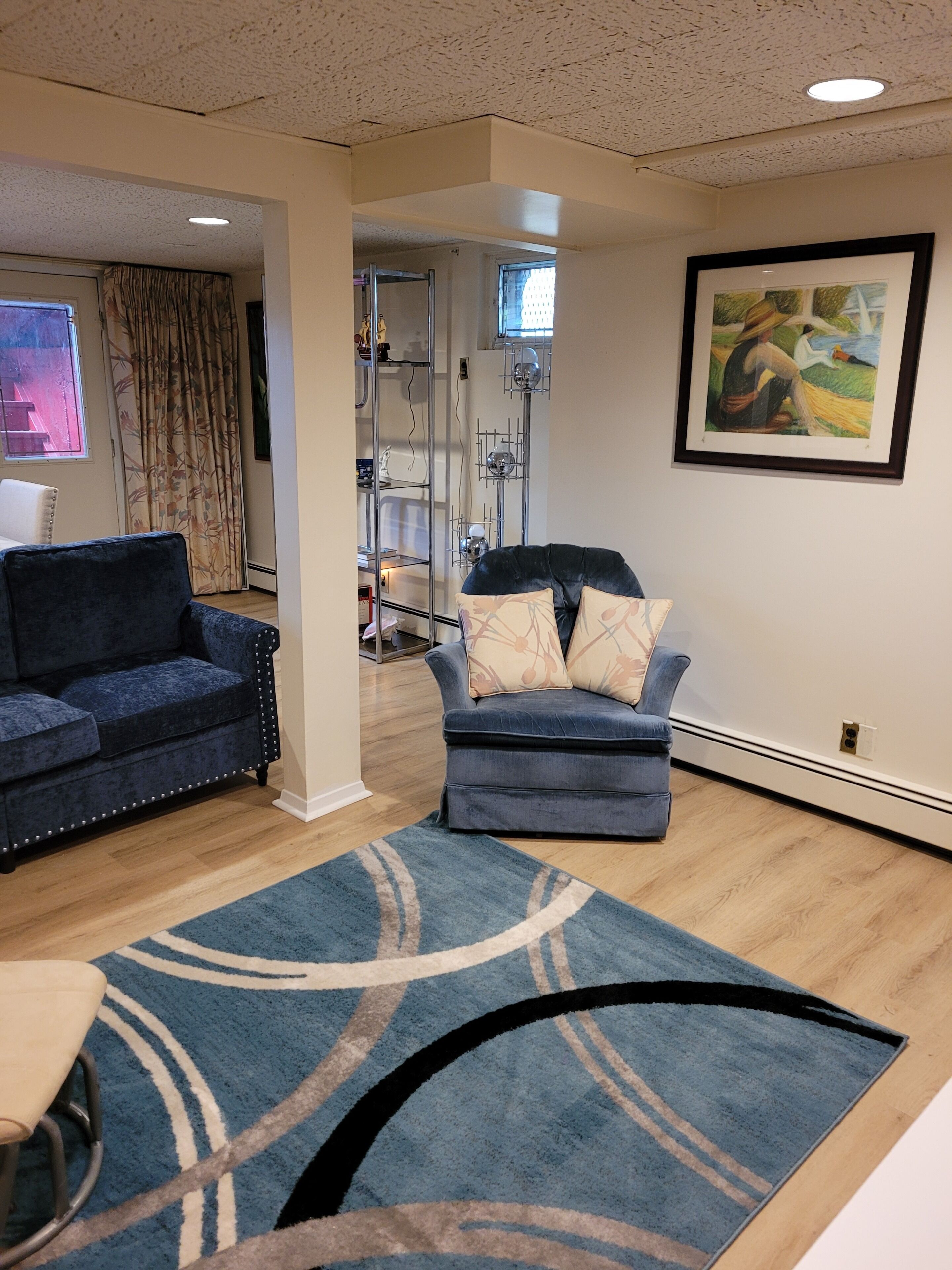 A living room with two sofas, a rug, a painting, and a staircase leading to another room.