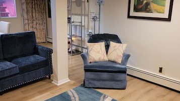 A living room with two sofas, a rug, a painting, and a staircase leading to another room.