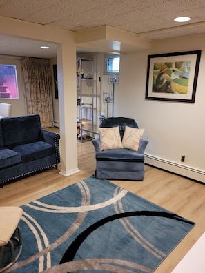 A living room with two sofas, a rug, a painting, and a staircase leading to another room.
