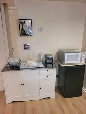 Une petite cuisine équipée d’un four à micro-ondes, d’un grille-pain et d’une machine à café, le tout posé sur un plan de travail noir.