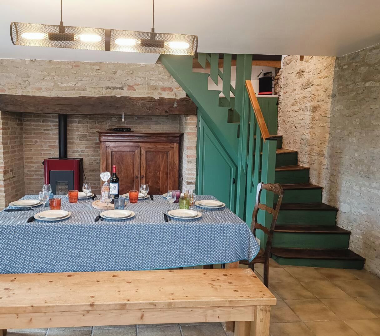 Un coin repas avec une table dressée pour quatre personnes, une cheminée et un escalier avec des rampes vertes.