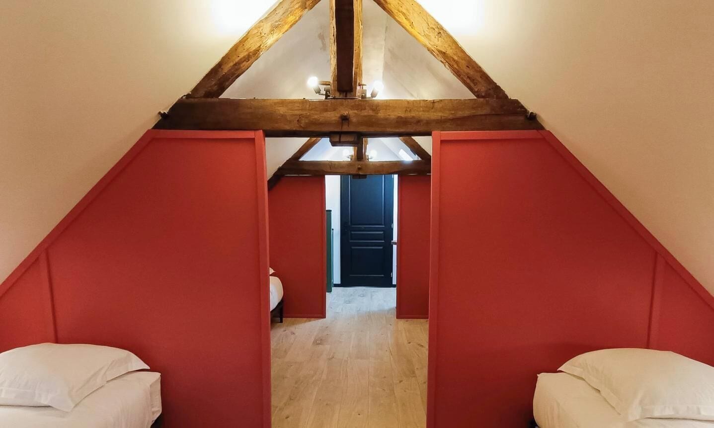 Een kamer met een schuine plafond, rode wanden en een zichtbare deur die naar een andere kamer leidt.