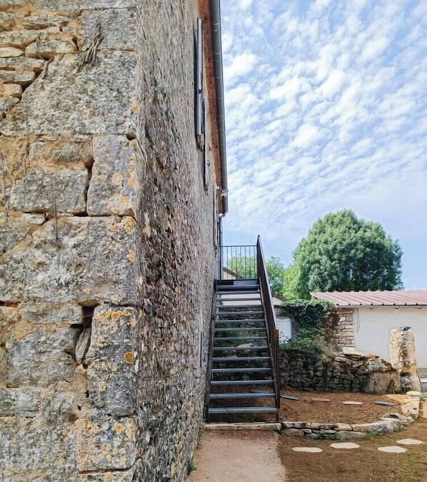 A stone building with a staircase leading to a balcony. - Oustalou Micro Farm (GRAMAT)