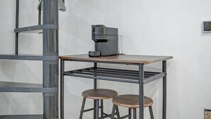 Pieni keittiönurkkaus, jossa on kahvinkeitin, metallihylly ja kaksi jakkaraa.