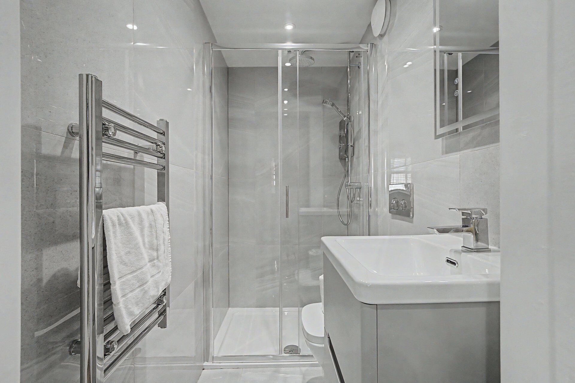 Een moderne badkamer met een glazen douchecabine, een wit wastafeltje en een handdoekhouder.
