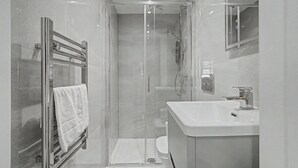 Ein modernes Badezimmer mit einer begehbaren Glasdusche, einem weißen Waschbecken und einem Handtuchhalter.