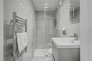 A modern bathroom with a glass-enclosed shower, a white sink, and a towel rack. - GuestReady - Chic City Studio in Vibrant Liverpool (Liverpool)