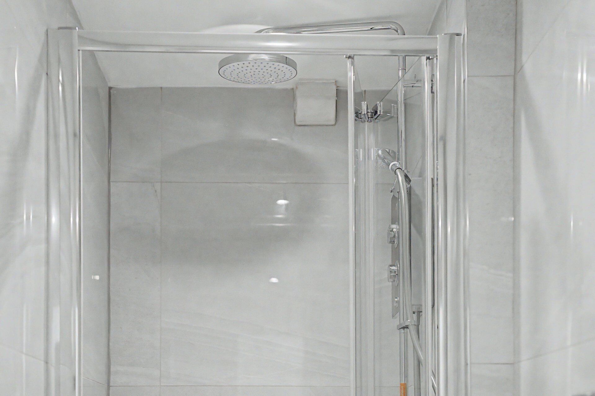 A clear glass shower enclosure with a handheld showerhead and a wall-mounted faucet.