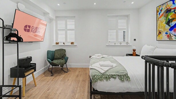 A bedroom with a bed, a chair, a TV, and a crib. - GuestReady - Modern 1bed in Liverpool (Liverpool)