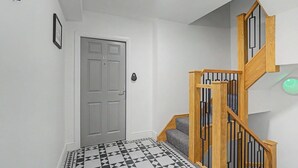 A hallway with a geometric patterned floor, a wooden staircase with black railings, and a door with a lock. - GuestReady - Modern 1bed in Liverpool (Liverpool)