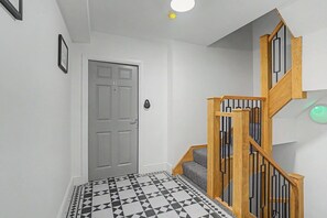 Ein Flur mit einem geometrisch gemusterten Boden, einer Holztreppe mit schwarzen Geländern und einer Tür mit Schloss.