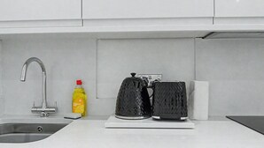 Ett kök med en diskho i rostfritt stål, en flaska diskmedel och två svarta kaffebryggare på bänkskivan.