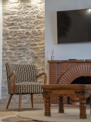 Eine Steinsäule, ein an der Wand befestigter Fernseher, ein gemustertes Sessel und ein Holztisch.