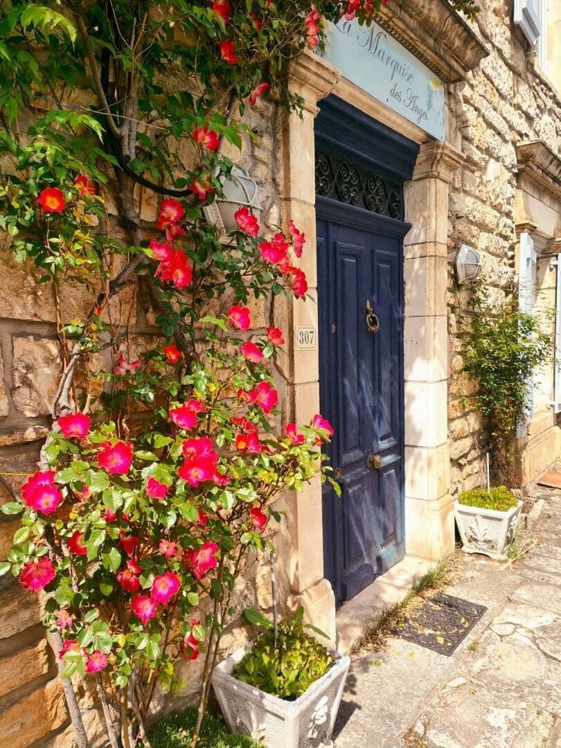 A stone building with a blue door, a sign above the door, and a flowering plant in front.