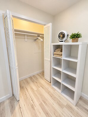 A walk-in closet with a hanging rod, shelves, and a fan.