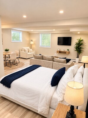 A modern hotel room with a large bed, a sofa, a dining table, and a TV.