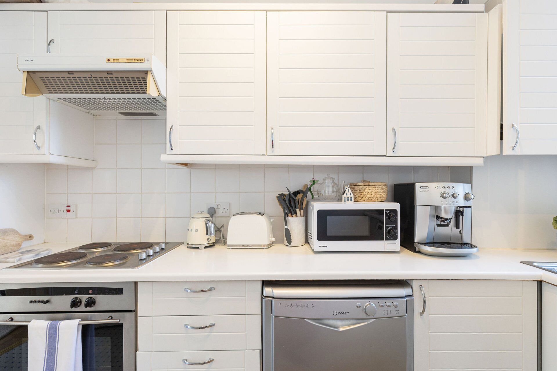 A kitchen with white cabinets, a stove, a microwave, a toaster, and a dishwasher.