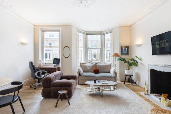 A modern living room with a sofa, coffee table, and a desk with a chair. - GuestReady - Charming Flat in Fulham, London (London)