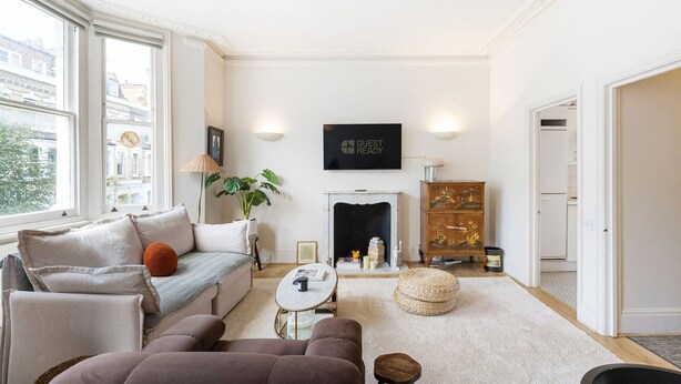 Una sala de estar con sofá, sillón, mesa de centro, chimenea, televisor y vistas a la ciudad a través de amplios ventanales.