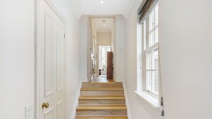 Un pasillo con paredes blancas, una escalera de madera y una ventana a la derecha.