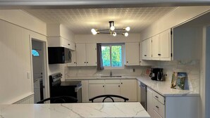 Eine moderne Küche mit weißen Schränken, einer Marmorarbeitsplatte, einem eingebauten Backofen und einem Fenster mit Blick auf Grünflächen.
