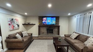Una sala de estar con dos sofás, una mesa de centro, una chimenea y un televisor montado encima.