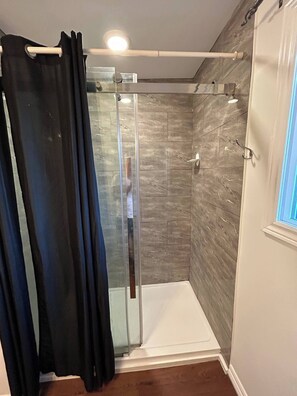 A shower area with a glass door, a towel rack, and a showerhead. - Cozy 3BR Cottage Near Lake Simcoe (Georgina)