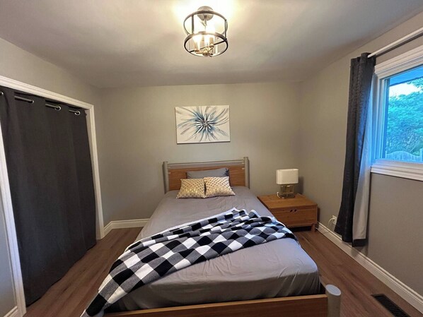 Un dormitorio con cama, mesita de noche, lámpara, ventana y lámpara del techo.