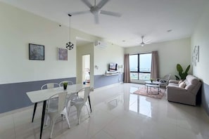 A modern living room with a dining area, a sofa, a TV, and a large window with a view. - Spacious 2BR Stay, 5 Mins from Jonker St (Malacca)