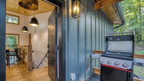 An outdoor kitchen area with a grill, wooden flooring, and a view of the surrounding forest. - Sauna, Cold Plunge, Hot Tub & Theater - Ellie Blue (Ellijay)