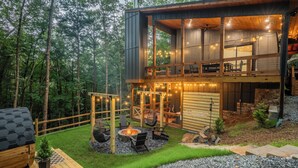 A modern two-story wooden cabin with a deck, a fire pit, and string lights. - Sauna, Cold Plunge, Hot Tub & Theater - Ellie Blue (Ellijay)