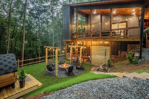 Eine moderne, zweistöckige Holzhütte mit einer Terrasse, einer Feuerstelle und Lichterketten.