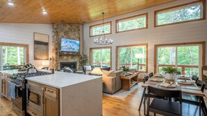 A spacious kitchen with a large island, a dining area with a wooden table, and a living room with a fireplace. - Sauna, Cold Plunge, Hot Tub & Theater - Ellie Blue (Ellijay)