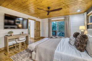 Un dormitorio con cama, escritorio, silla, ventilador de techo y ventana con cortinas.