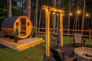 Una cabaña de madera rústica con entrada abovedada, una silla colgante, un brasero y luces de cuerda.